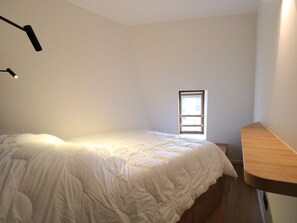 A bedroom with a bed, a window, and a desk.