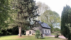 Een huis met een schuin dak, schoorsteen en een klein terras met een bankje.