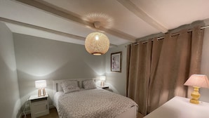 Een slaapkamer met een bed, twee nachtkastjes met lampen, een plafondventilator en een raam met gordijnen.