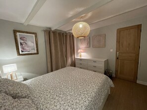 A bedroom with a bed, a dresser, a door, and a hanging light fixture. - Charming cottage classified 4 * (Le Torquesne)