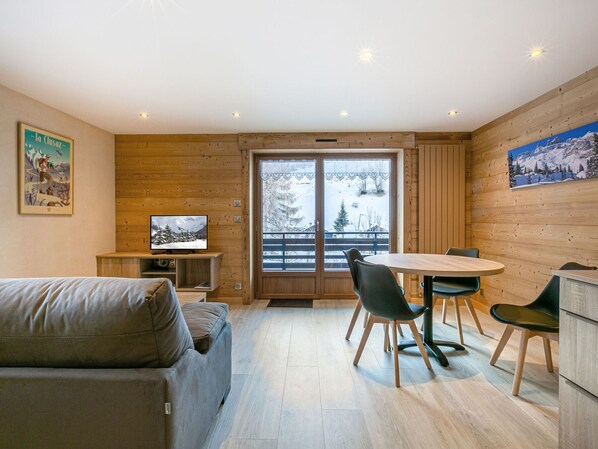 A modern interior with a sofa, dining table, chairs, a TV, and a large window with a snowy view.