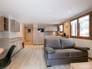 A compact living space with a kitchenette, a sofa, a dining table, and a window with a view.