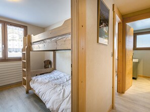 A bunk bed room with a wooden ladder, a small chair, and a window with curtains.