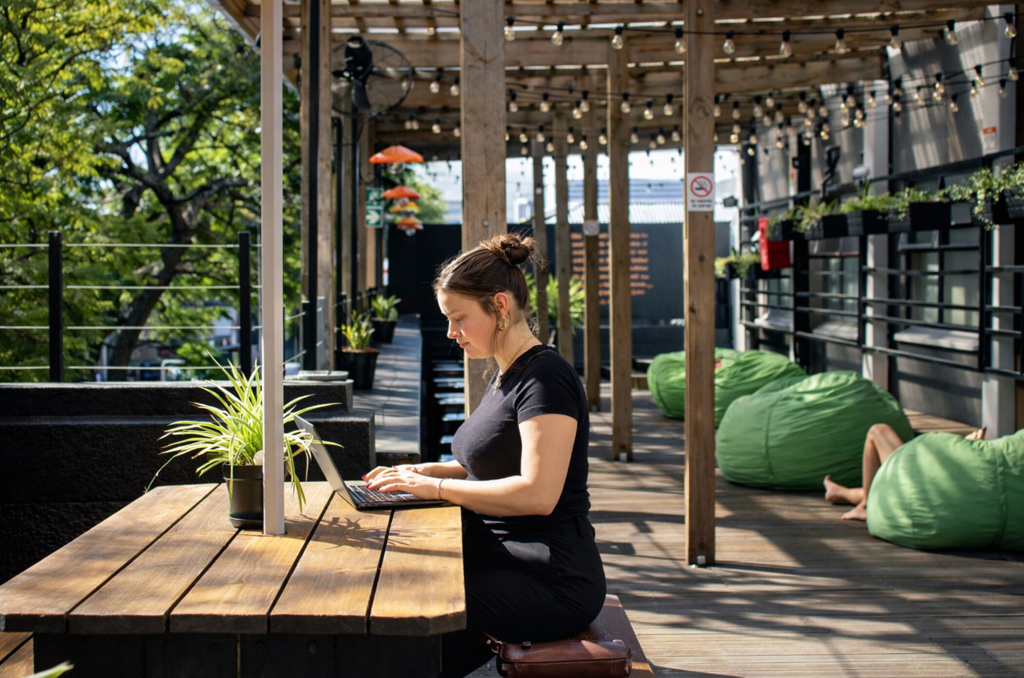 A person working on a laptop at a wooden table with potted plants nearby.