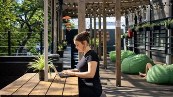 A person working on a laptop at a wooden table with potted plants nearby.