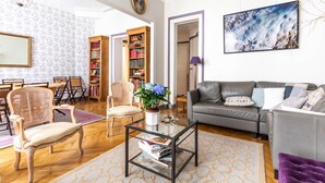A spacious living room with a grey sofa, wooden chairs, a glass coffee table, and a bookshelf. - Vintage Violet, by Veeve (Paris)