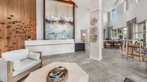 Un área de recepción moderna con un muro de madera, una mesa de recepción, un sofá blanco y un comedor con muebles de madera.