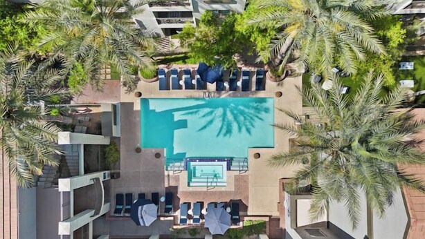 Vista aérea de un hotel con piscina central rodeada de palmeras, sillas de descanso y un bar junto a la piscina.