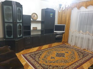 Un salon avec un grand meuble en bois foncé, un téléviseur à écran plat, un tapis à motifs et un lustre.