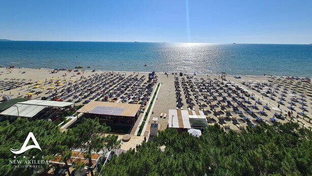 A beach hotel with rows of sunbeds and umbrellas, a pool area, and a view of the sea. - New Akileda Hotel (Golem)