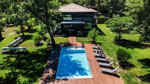 Une piscine avec une terrasse en bois, entourée de chaises longues et une maison en arrière-plan.