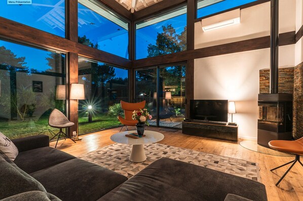 A modern living room with a large glass wall, a fireplace, and a cozy seating area.