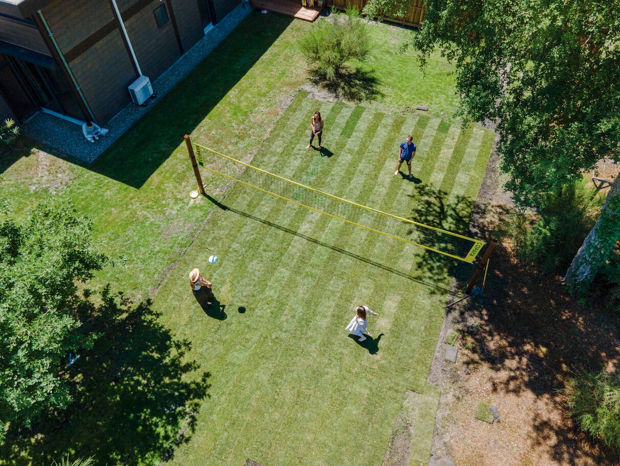An aerial view of a backyard with a volleyball net, a small tree, and a grassy area.