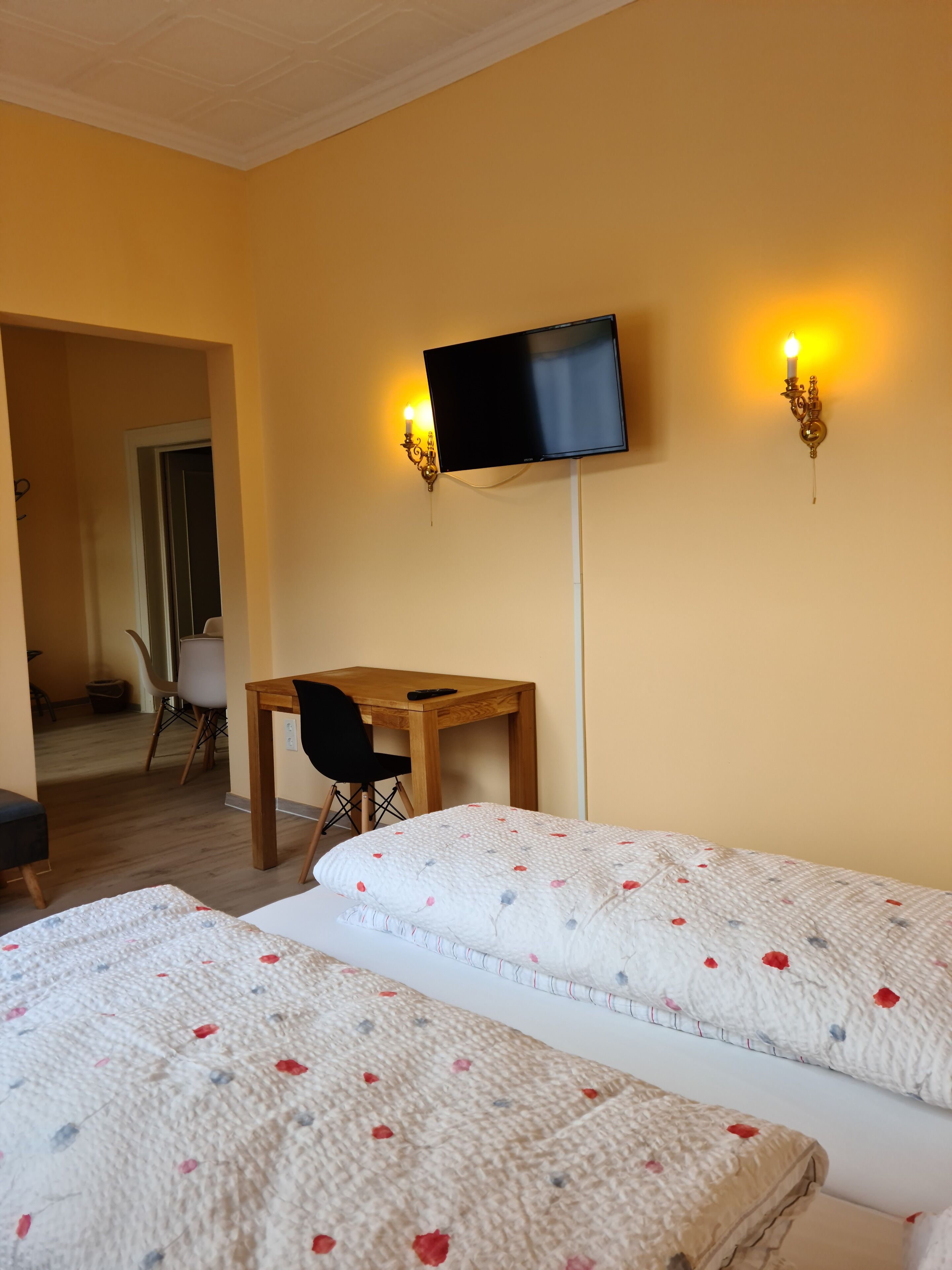 Habitación de hotel con dos camas, un escritorio, una silla, un televisor montado en la pared y una puerta que da a otra habitación.