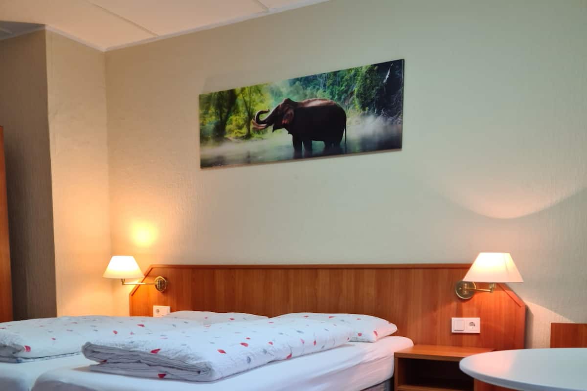 Een hotelkamer met een tweepersoonsbed, twee bedlampen, een kleine tafel en een schilderij van een olifant aan de muur.