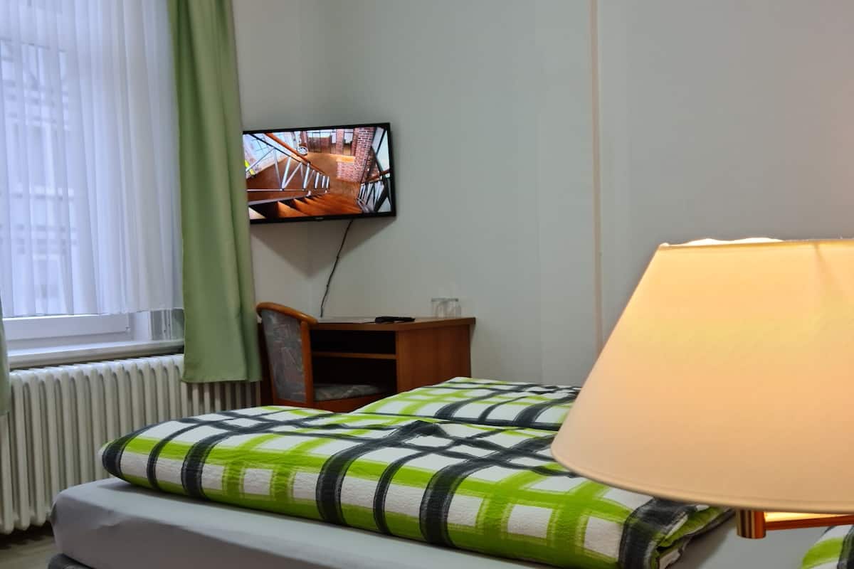 Een hotelkamer met een bed, een aan de muur bevestigde televisie, een lamp en een raam met gordijnen.