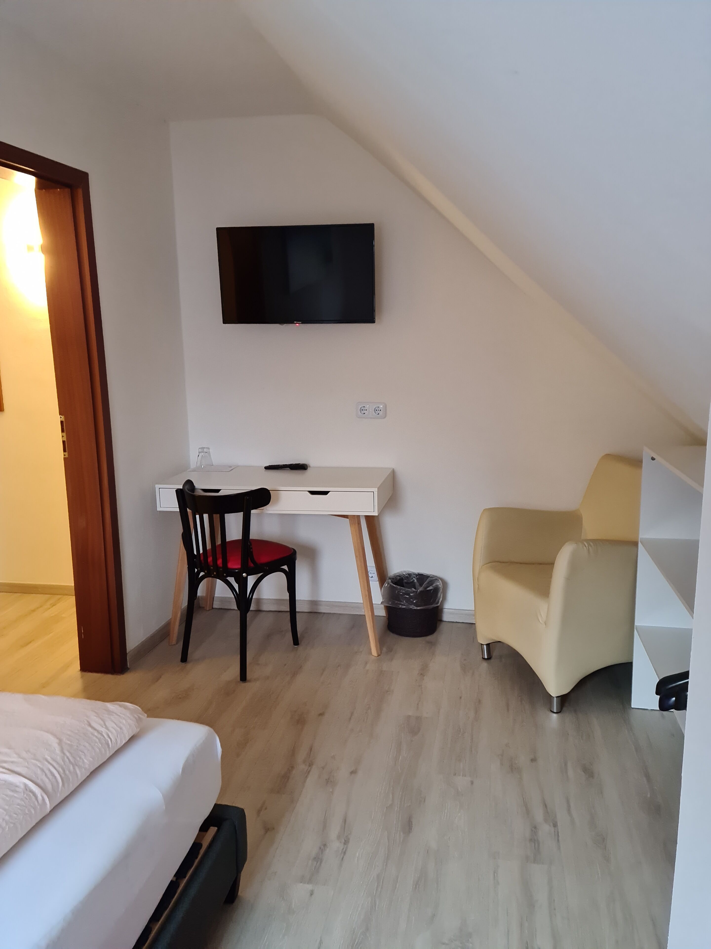 Ein kleiner, gut beleuchteter Raum mit einem Bett, einem Schreibtisch mit Stuhl, einem an der Wand befestigten Fernseher und einem Sofa.
