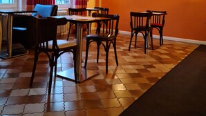 A dining area with a patterned floor, orange walls, and a ceiling with a grid design. - Pension Kreihe (Bad Lauterberg)