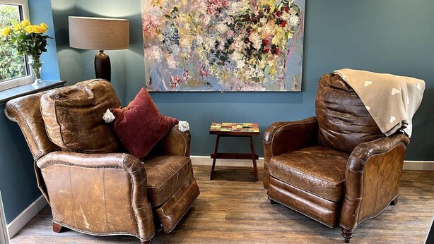 A living room with two brown leather armchairs, a large floral painting on the wall, a small table with books, and a lamp. - Freshwater - Hot Tub - Pet Friendly - Garden (Freshwater)