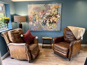 A living room with two brown leather armchairs, a large floral painting on the wall, a small table with books, and a lamp. - Freshwater - Hot Tub - Pet Friendly - Garden (Freshwater)