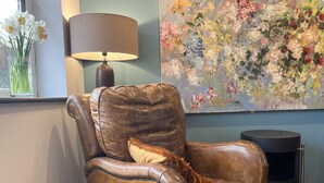 A brown leather armchair with a frayed pillow, a floor lamp, and a floral painting on the wall. - Freshwater - Hot Tub - Pet Friendly - Garden (Freshwater)