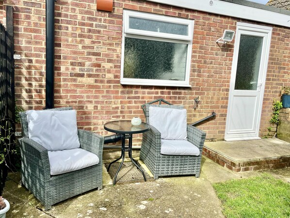 A patio with two wicker chairs and a small round table, a brick wall, a white door, and a window with frosted glass. - Freshwater - Hot Tub - Pet Friendly - Garden (Freshwater)