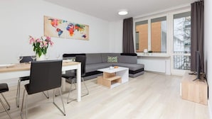 Ein modernes Wohnzimmer mit Essbereich, einem grauen Sofa, einem Couchtisch und einem Fernseher auf einem Holzboden.