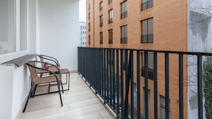 Ein Balkon mit schwarzem Metallgeländer, einem Korbstuhl und einem kleinen Tisch.