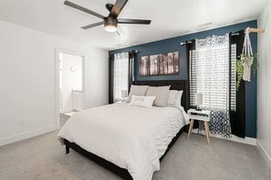 A bedroom with a bed, a ceiling fan, a nightstand, a lamp, and a window with patterned curtains. - Modern and cozy family home with 3 bedrooms (Chubbuck)