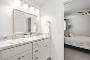 A bathroom with two sinks, a large mirror, and a bed visible through an open door. - Modern and cozy family home with 3 bedrooms (Chubbuck)