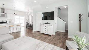 Una cocina moderna con armarios blancos, un comedor con mesa y sillas, y una sala de estar con sofá y televisor.