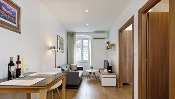 A modern living room with a sofa, a dining table, and a TV. There is a window with curtains, a door, and a small table with a plant. - Dominus, Modernly Decorated Suite in City Center (Split)