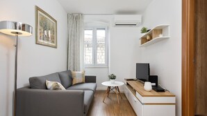 A compact living space with a grey sofa, a small round table, a TV, and a wooden desk. - Dominus, Modernly Decorated Suite in City Center (Split)