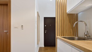 A narrow hallway with a wooden door, a black door, and a kitchen area with a stainless steel sink and wooden countertop. - Dominus, Modernly Decorated Suite in City Center (Split)
