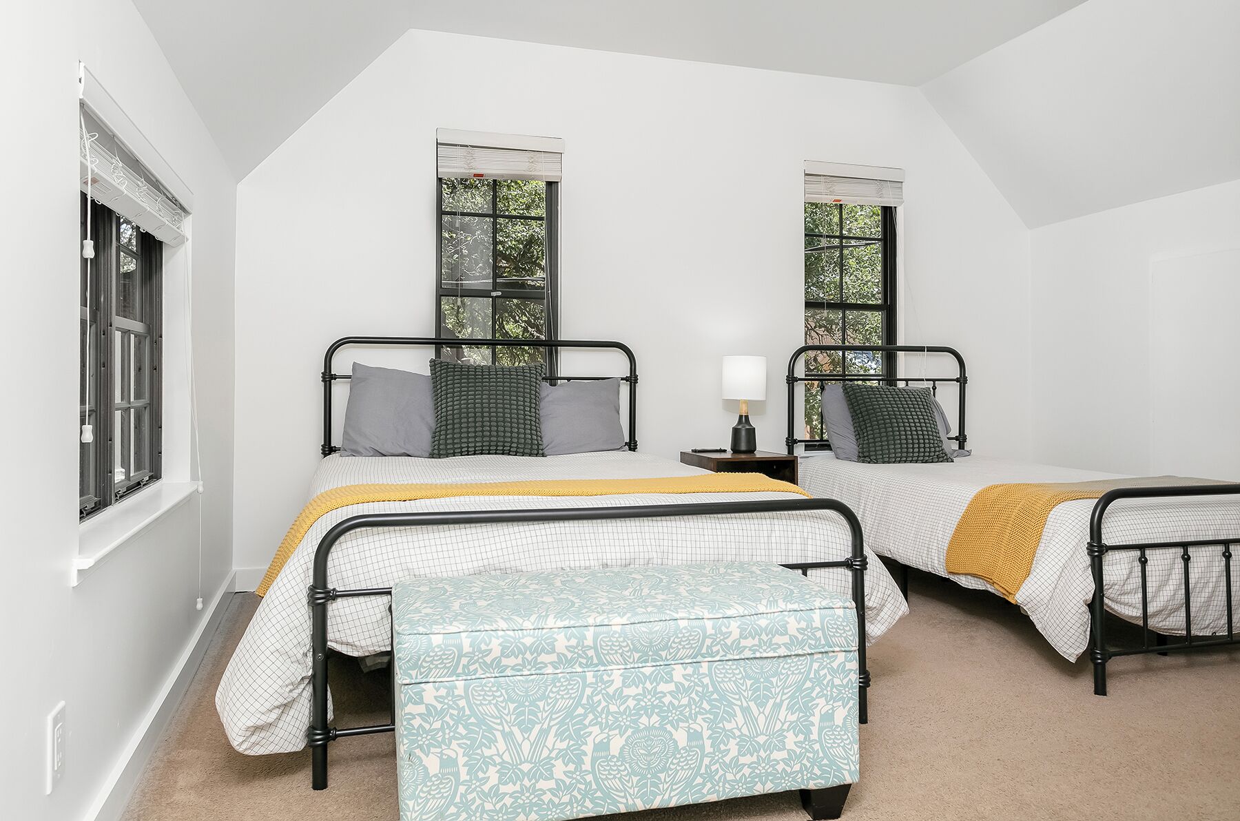 A bedroom with two beds, a bench, and a nightstand with a lamp.
