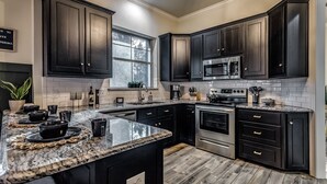 A modern kitchen with dark cabinetry, granite countertops, stainless steel appliances, and a window providing natural light. - 5Bdrm 3Ba Posh Lake Texoma Home (Pottsboro)