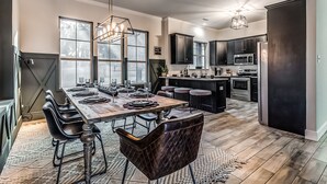 A modern kitchen with dark cabinetry, a central island, and a dining area with a long table and chairs. - 5Bdrm 3Ba Posh Lake Texoma Home (Pottsboro)
