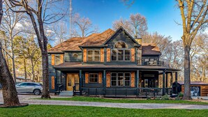 A two-story log cabin with a wrap-around porch, large windows, and a prominent chimney. - 5Bdrm 3Ba Posh Lake Texoma Home (Pottsboro)