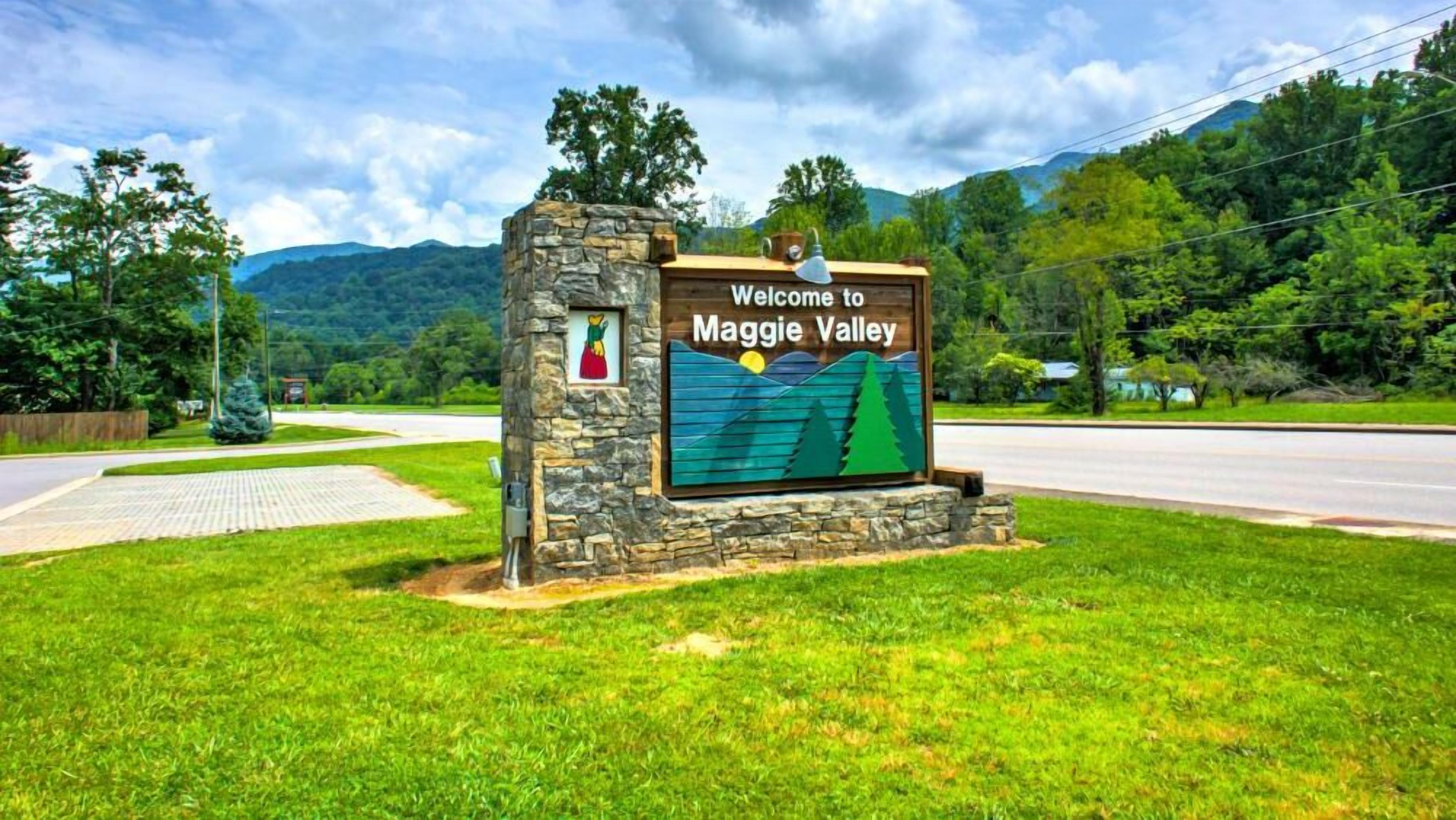 A welcome sign for Maggie Valley with a scenic view of mountains and a paved road.