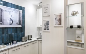 A modern kitchen with white cabinets, a blue backsplash, and a glass shelf with decorative items. - Host Inn - Sweet Croisette (Cannes)