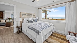 A bedroom with a bed, a nightstand, a lamp, a ceiling fan, a window with a view of the beach, and a view of the ocean. - Private Coastal Haven - 2nd Row, Spectacular views (Emerald Isle)