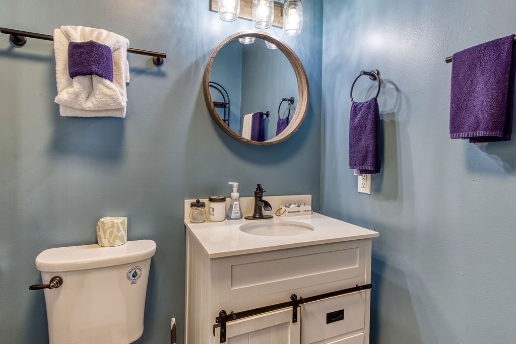 A bathroom with a toilet, sink, and mirror. There are towels hanging on a rack and a soap dispenser on the sink.
