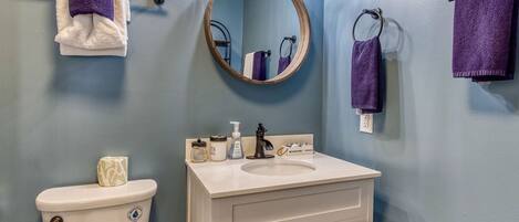 A bathroom with a toilet, sink, and mirror. There are towels hanging on a rack and a soap dispenser on the sink.