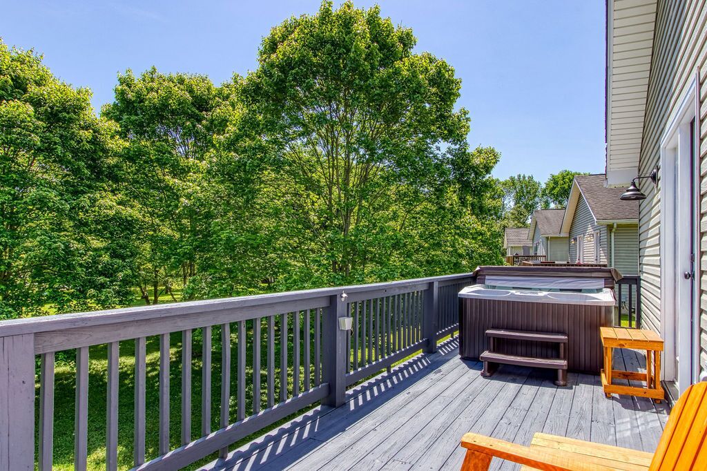 A deck with a hot tub, wooden furniture, and a view of a forested area.