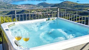 Un jacuzzi con dos copas de vino, con vistas a un paisaje costero con colinas y al mar.