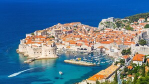 Una ciudad costera con arquitectura histórica, un puerto con barcos y una muralla fortificada.