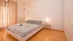 Ein Schlafzimmer mit einem Bett, Nachttischlampen, einem Nachttisch und einem Fenster mit Vorhängen.