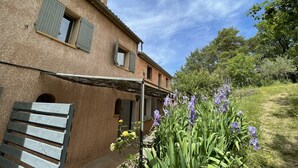 Une maison de campagne avec un porche abrité et un jardin où poussent des fleurs violettes.