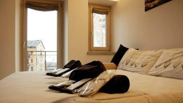 A hotel room with a bed, a window, and a view of buildings outside. - SUPERIOR SUITE, Verona | 1K_HOME (Bosco Chiesanuova)