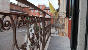 A metal balcony railing with a view of buildings and a flag. - SUPERIOR SUITE, Verona | 1K_HOME (Bosco Chiesanuova)